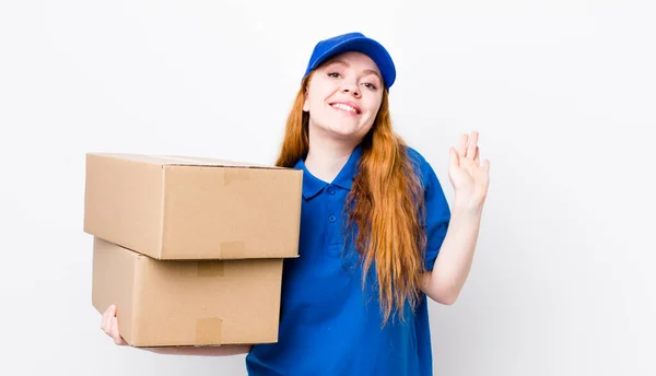 幸せそうに笑って手を振って歓迎し挨拶する赤い頭の女性 配送ボックスのコンセプト — ストック写真