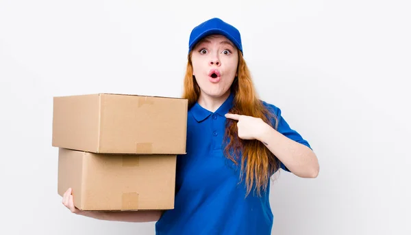 赤い頭のかなりの女性がショックを受けて 口を大きく開いて驚いて 自分自身を指している 配送ボックスのコンセプト — ストック写真