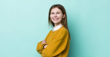 Kızıl saçlı güzel kadın kameraya çapraz kollarıyla gülümsüyor ve mutlu, kendinden emin, tatmin olmuş bir yüz ifadesi var.