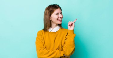 Kızıl saçlı güzel kadın mutlu bir şekilde gülümsüyor ve yan bakıyor, merak ediyor, düşünüyor ya da bir fikri var.