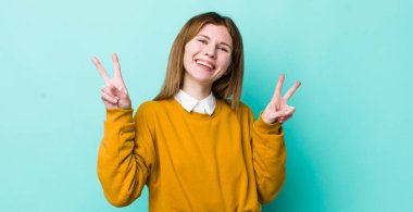 kızıl saçlı güzel kadın gülümsüyor ve mutlu görünüyor, arkadaş canlısı ve memnun, işaret eden zafer ya da huzur iki elinle