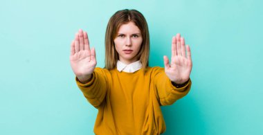 Kızıl saçlı güzel kadın ciddi, mutsuz, kızgın ve hoşnutsuz görünüyor. Girmeyi yasaklıyor ya da her iki avucunun içinde de dur diyor.