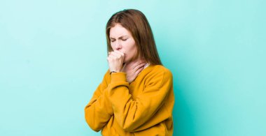 Kızıl saçlı güzel bir kadın boğazı ağrıyan ve grip belirtileri gösteren ağzı kapalı öksüren bir hasta.