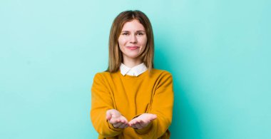 kızıl saçlı güzel kadın mutlu bir şekilde gülümsüyor, arkadaş canlısı, kendinden emin, pozitif bakışlı, bir nesne ya da konsept sunuyor ve gösteriyor.