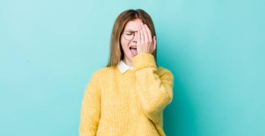 Kızıl saçlı güzel bir kadın uykulu, sıkılmış ve esniyor, baş ağrısı ve yüzünün yarısını kaplayan bir eliyle