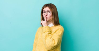 Kızıl saçlı güzel bir kadın sessizlik ve sessizlik istiyor, parmaklarıyla ağzının önünde işaret ediyor, 