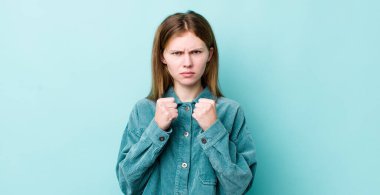 Kızıl saçlı güzel bir kadın kendine güvenen, sinirli, güçlü ve agresif görünüyor. Yumrukları boks pozisyonunda dövüşmeye hazır.