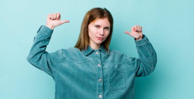 Kızıl saçlı güzel bir kadın gururlu, kibirli ve kendinden emin, tatmin olmuş ve başarılı görünüyor, kendini işaret ediyor.