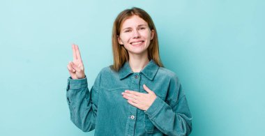 Kızıl saçlı güzel bir kadın mutlu, kendine güvenen ve güvenilir görünüyor, gülümsüyor ve zafer işareti gösteriyor, olumlu bir tavırla.