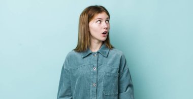 Kızıl saçlı güzel kadın şaşkın, mutlu, şaşkın ve şaşırmış hissediyor, ağzı açık bir şekilde yana bakıyor.