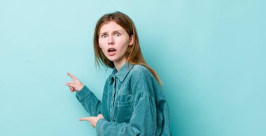 Kızıl saçlı, güzel bir kadın şaşkın ve şaşırmış hissediyor. Yandaki fotokopi alanını işaret ediyor. Şaşırmış ve ağzı açık bakıyor.