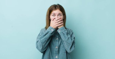 Kızıl saçlı, güzel bir kadın elleri ile ağzını kapatıyor, şok olmuş, şaşırmış bir ifadeyle, sır saklıyor ya da 