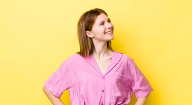 kızıl saçlı güzel bir kadın mutlu, neşeli ve kendinden emin görünüyor, gururla gülümsüyor ve iki elini de kalçasında istiyor.