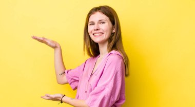 kızıl saçlı güzel kadın gülümsüyor, mutlu, pozitif ve tatmin olmuş hissediyor, fotokopi alanında nesne ya da konsept tutuyor ya da gösteriyor