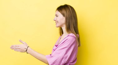 Kızıl saçlı güzel kadın gülümsüyor, seni selamlıyor ve başarılı bir anlaşma için el sıkışmayı teklif ediyor, işbirliği konsepti.