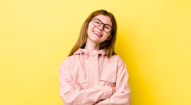 Kızıl saçlı güzel bir kadın kollarını kavuşturup mutlu bir şekilde gülüyor, rahat, pozitif ve tatmin edici bir pozla.