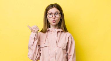 Kızıl saçlı güzel bir kadın inançsızlıktan şaşkın şaşkın bakıyor, yan taraftaki objeyi işaret ediyor ve 