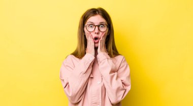 Kızıl saçlı güzel kadın şok olmuş ve korkmuş hissediyor, ağzı açık ve elleri yanaklarında korkmuş görünüyor.