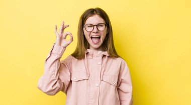 Kızıl saçlı güzel bir kadın kendini başarılı ve tatmin olmuş hissediyor, ağzı açık gülümsüyor, elle işaret veriyor.