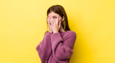 Kızıl saçlı, güzel bir kadın korkmuş ya da utanmış hissediyor, gözleri yarı kapalı ya da elleri kapalı gözetliyor.