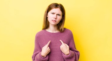 Kızıl saçlı güzel bir kadın, şaşkın ve şaşkın bir bakışla kendini işaret ediyor. Seçildiğine şaşırmış ve şaşırmış.