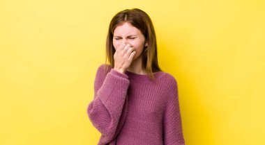 Kızıl saçlı güzel kadın iğreniyor, pis ve nahoş bir koku duymamak için burnunu tutuyor.