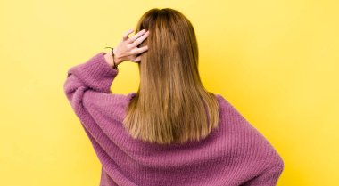 Kızıl saçlı güzel bir kadın bilgisiz ve kafası karışık, bir çözüm düşünüyor, eli kalçasında, diğeri kafasında, dikiz aynasından.