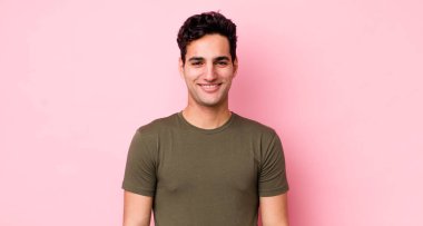 Yakışıklı İspanyol adam kameraya çapraz kollarıyla gülümsüyor ve mutlu, kendinden emin, tatmin olmuş bir yüz ifadesi var.