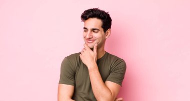 Yakışıklı İspanyol adam mutlu, kendinden emin bir ifadeyle gülümsüyor elleri çenesinde, merak ediyor ve yan tarafa bakıyor.