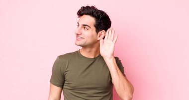 Yakışıklı İspanyol adam gülümsüyor, tuhaf bir şekilde yan tarafa bakıyor, dedikoduları dinlemeye ya da bir sırrı duymaya çalışıyor.