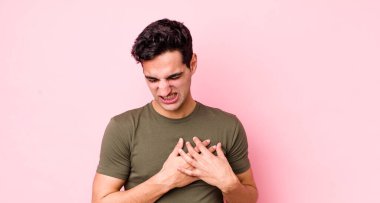 Yakışıklı İspanyol adam üzgün, yaralı ve kalbi kırık görünüyor, iki elini de kalbe yakın tutuyor, ağlıyor ve depresif hissediyor.