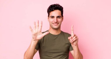 Yakışıklı İspanyol adam gülümsüyor ve arkadaş canlısı görünüyor, 6 ya da 6 numarayı gösteriyor, elleri önde, geriye doğru sayıyor.