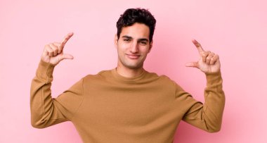 Yakışıklı İspanyol bir adam kendi gülüşünü çiziyor ya da özetliyor iki eliyle, olumlu ve mutlu görünüyor, sağIık kavramı.