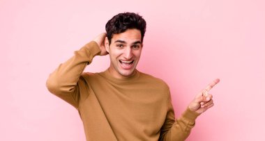 Yakışıklı İspanyol adam gülüyor, mutlu, pozitif ve şaşırmış görünüyor, yanal fotokopi alanını işaret eden harika bir fikrin farkına varıyor.