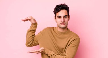 Yakışıklı İspanyol bir adam iki eliyle bir objeyi tutuyor fotokopi alanında, bir nesneyi gösteriyor, sunuyor ya da reklamını yapıyor.