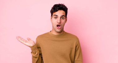 Yakışıklı İspanyol adam şaşırmış ve şoka uğramış görünüyor, çenesi düşmüş, bir objeyi elinde açık bir elle tutuyor.