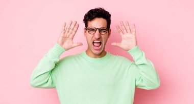 Yakışıklı İspanyol adam panik ya da öfke içinde bağırıyor, şok olmuş, korkmuş ya da öfkeli, elleri başının yanında.