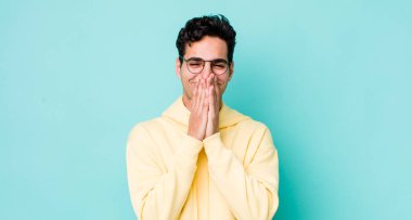 Yakışıklı İspanyol adam mutlu, neşeli, şanslı ve şaşkın görünüyor iki eliyle ağzını kapatıyor.