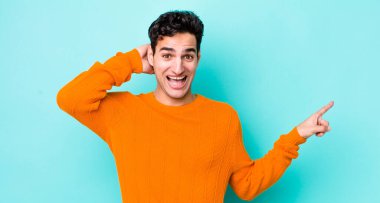 Yakışıklı İspanyol adam gülüyor, mutlu, pozitif ve şaşırmış görünüyor, yanal fotokopi alanını işaret eden harika bir fikrin farkına varıyor.