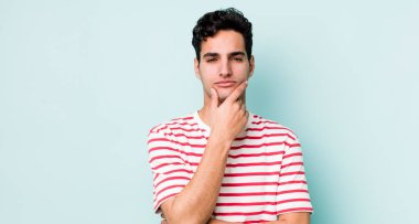 Yakışıklı İspanyol bir adam ciddi, düşünceli ve güvensiz görünüyor, bir kolu çapraz ve çene üzerinde, seçenekleri tartıyor