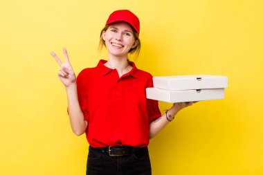 Kızıl saçlı güzel kadın gülümsüyor ve arkadaş canlısı görünüyor, iki numarayı gösteriyor. Pizza dağıtımı kavramı