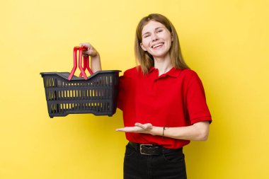 kızıl saçlı güzel bir kadın neşeli bir şekilde gülümsüyor, mutlu hissediyor ve bir konsept gösteriyor. Alışveriş sepeti konsepti