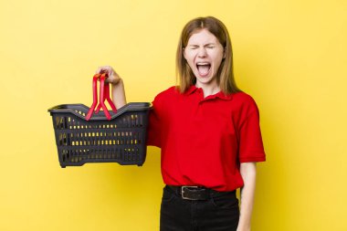 Kızıl saçlı, güzel bir kadın agresif bir şekilde bağırıyor, çok kızgın görünüyor. Alışveriş sepeti konsepti