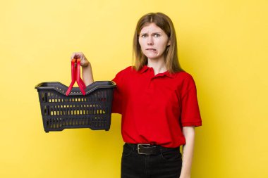 Kızıl saçlı güzel kadın kafası karışık ve şaşkın görünüyor. Alışveriş sepeti konsepti