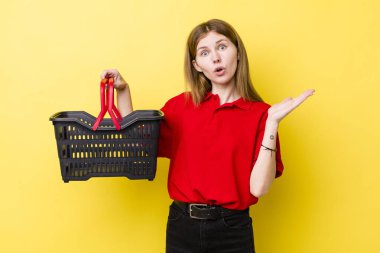 Kızıl saçlı, güzel bir kadın şaşırmış ve şok olmuş görünüyor. Çenesi düşmüş, elinde bir nesne var. Alışveriş sepeti konsepti