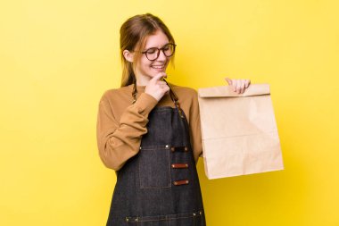 Kızıl saçlı, güzel bir kadın mutlu, kendinden emin, elleri çenesinde gülümsüyor. teslimat paket servis kavramı