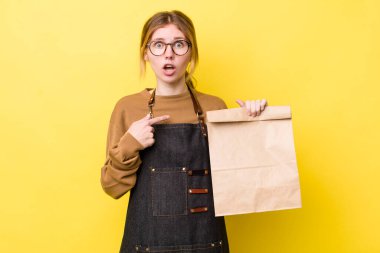 Kızıl saçlı güzel kadın şok olmuş ve ağzı açık, kendini işaret eden bir şekilde şaşırmış görünüyor. teslimat paket servis kavramı