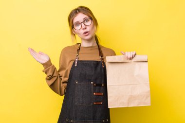 Kızıl saçlı, güzel bir kadın şaşırmış ve şok olmuş görünüyor. Çenesi düşmüş, elinde bir nesne var. teslimat paket servis kavramı