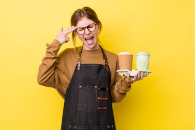 Kızıl saçlı güzel bir kadın mutsuz ve stresli görünüyor, intihar jesti silah işareti yapıyor. kahve konseptini kaldır.