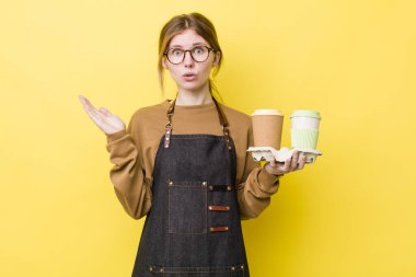 Kızıl saçlı, güzel bir kadın şaşırmış ve şok olmuş görünüyor. Çenesi düşmüş, elinde bir nesne var. kahve konseptini kaldır.